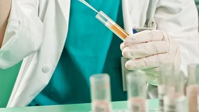 Person med hansker holder reagensrør og pipetterer væske i laboratoriemiljø