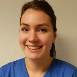 Smilende kvinne i blå veterinæruniform foran lys vegg.